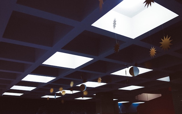 Photograph of paper suns and moons hanging from strings attached to an intermittently lit drop ceiling.